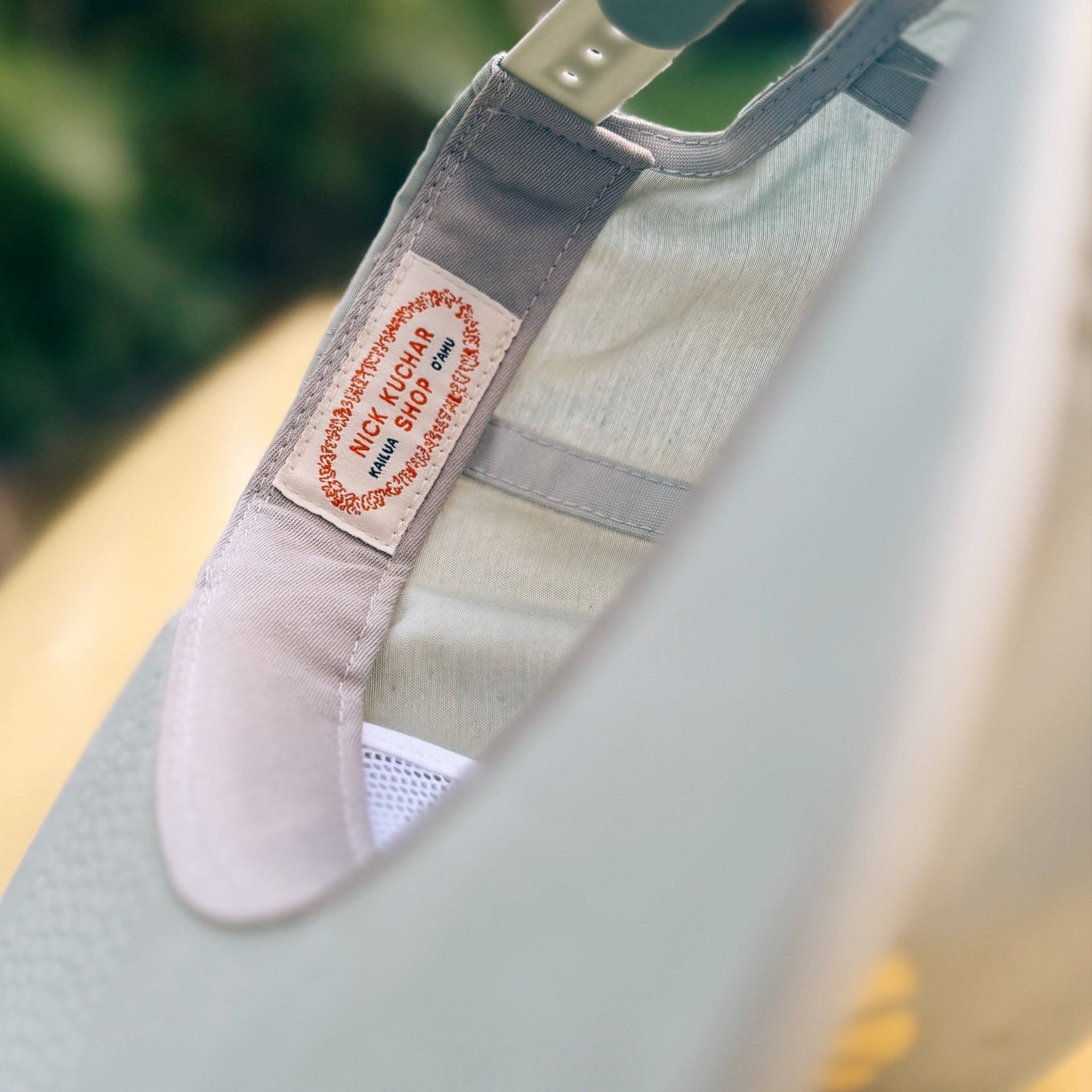 Light gray cap with a nick kuchar brand label on a blurred green and yellow background