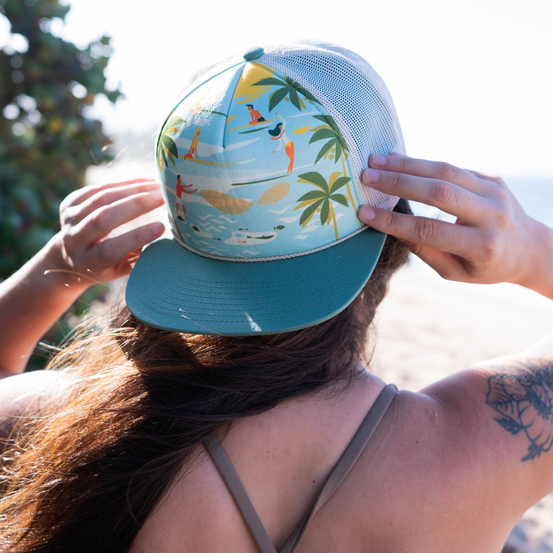 Person wearing a colorful cap with palm trees and surfers on a sunny day.