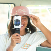woman wearing hat with aloha text and holding super 8 camera