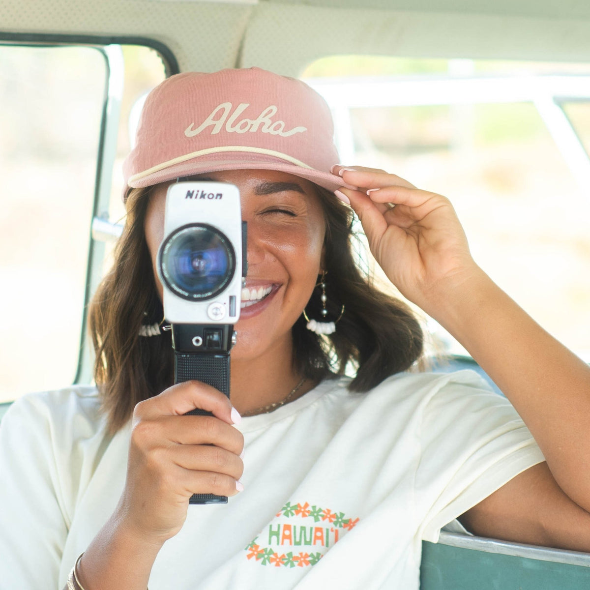 woman wearing hat with aloha text and holding super 8 camera