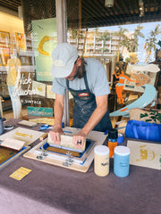 artist printing at a counter with various items including a blue ink container and a yellow ink container.