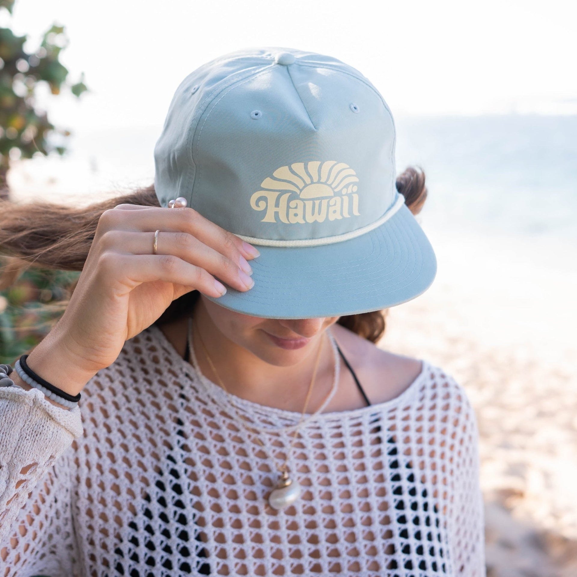 Person wearing a light blue cap with 'Hawaii' printed on it, outdoors.