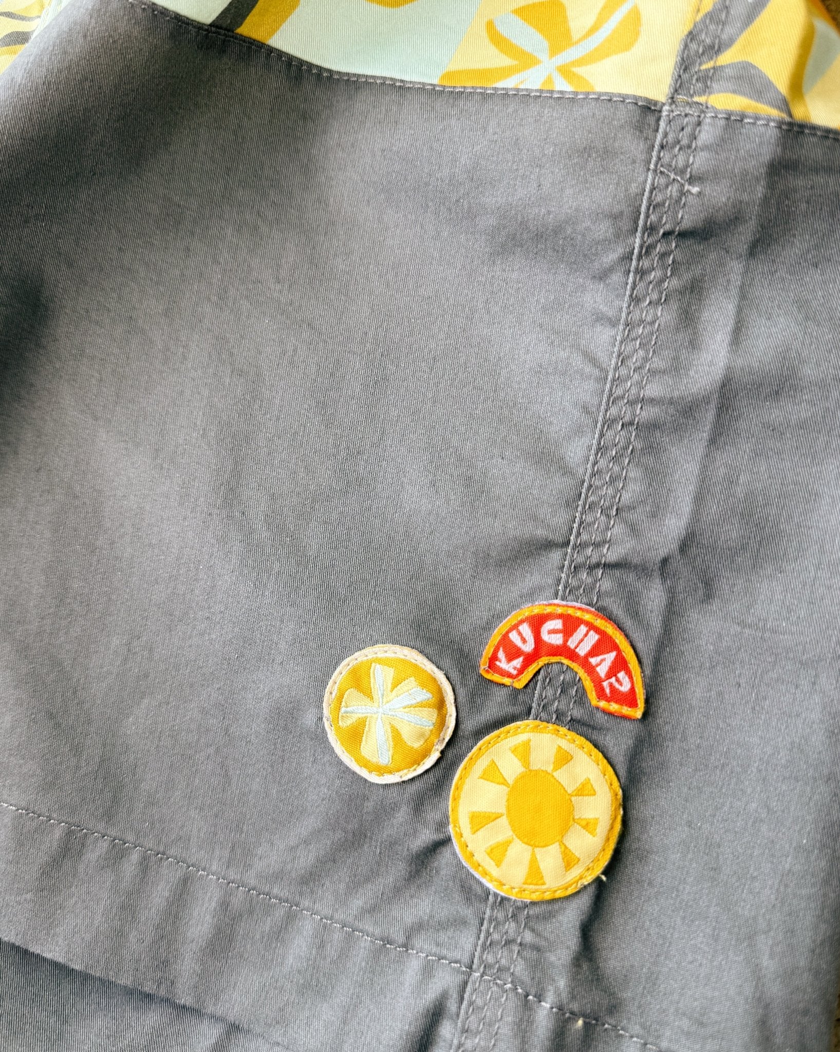 Gray brown fabric with colorful patches including a sun design and 'Kuchar' branding.