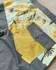 Close-up of boardshorts with colorful pattern and a button, on a neutral background.