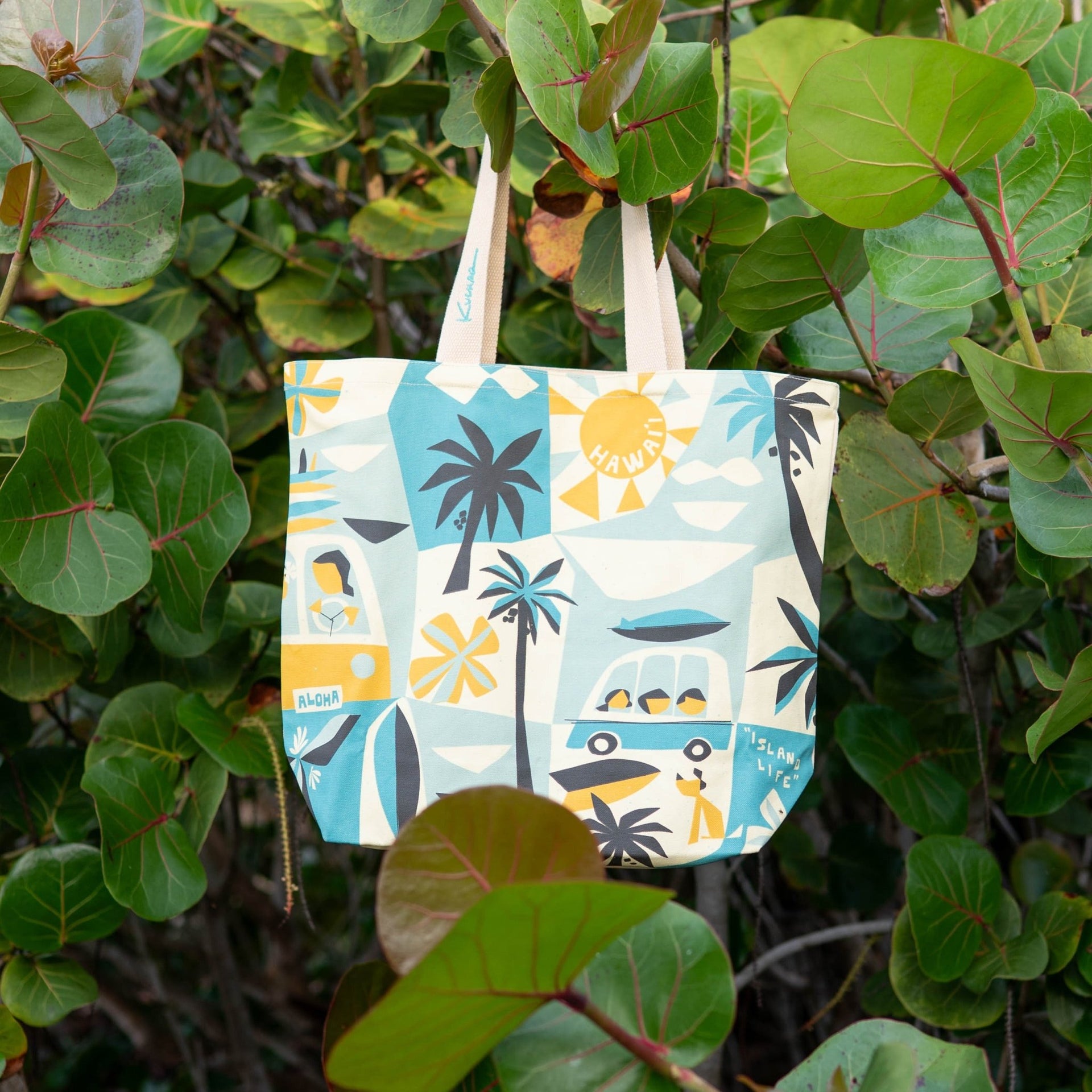 Colorful beach bag with a tropical pattern hanging from green leaves