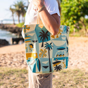 Person holding a colorful tote bag with beach-themed design outdoors.