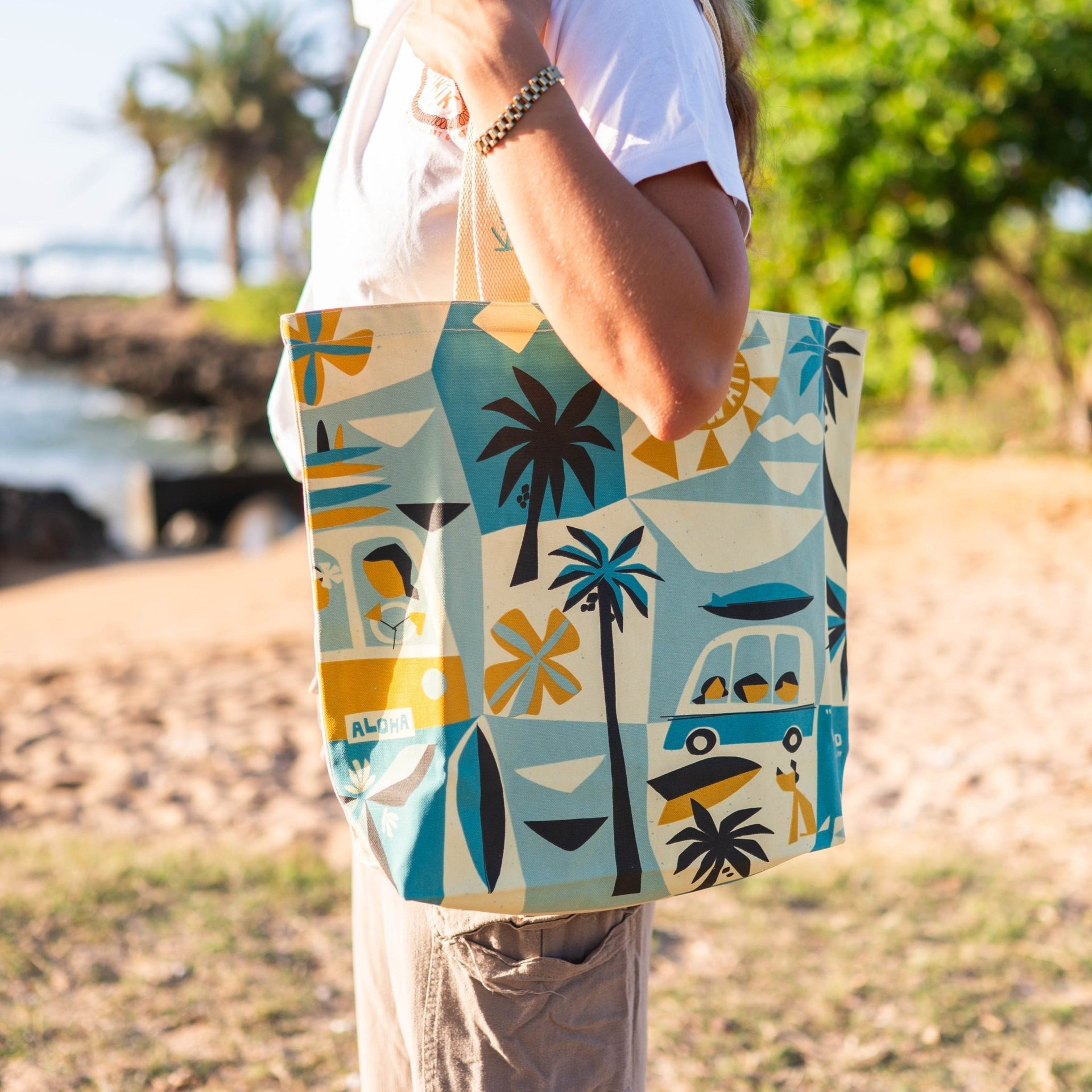 Person holding a colorful tote bag with beach-themed design outdoors.