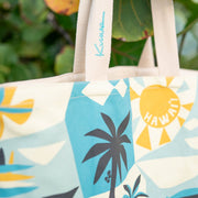 Beige tote bag with tropical design and 'Kauai' branding, hanging on a tree branch.