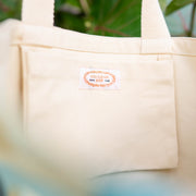 Beige tote bag with a visible brand label against a natural background