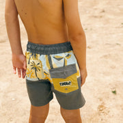 Child wearing a colorful swimsuit with a brand logo on a sandy background