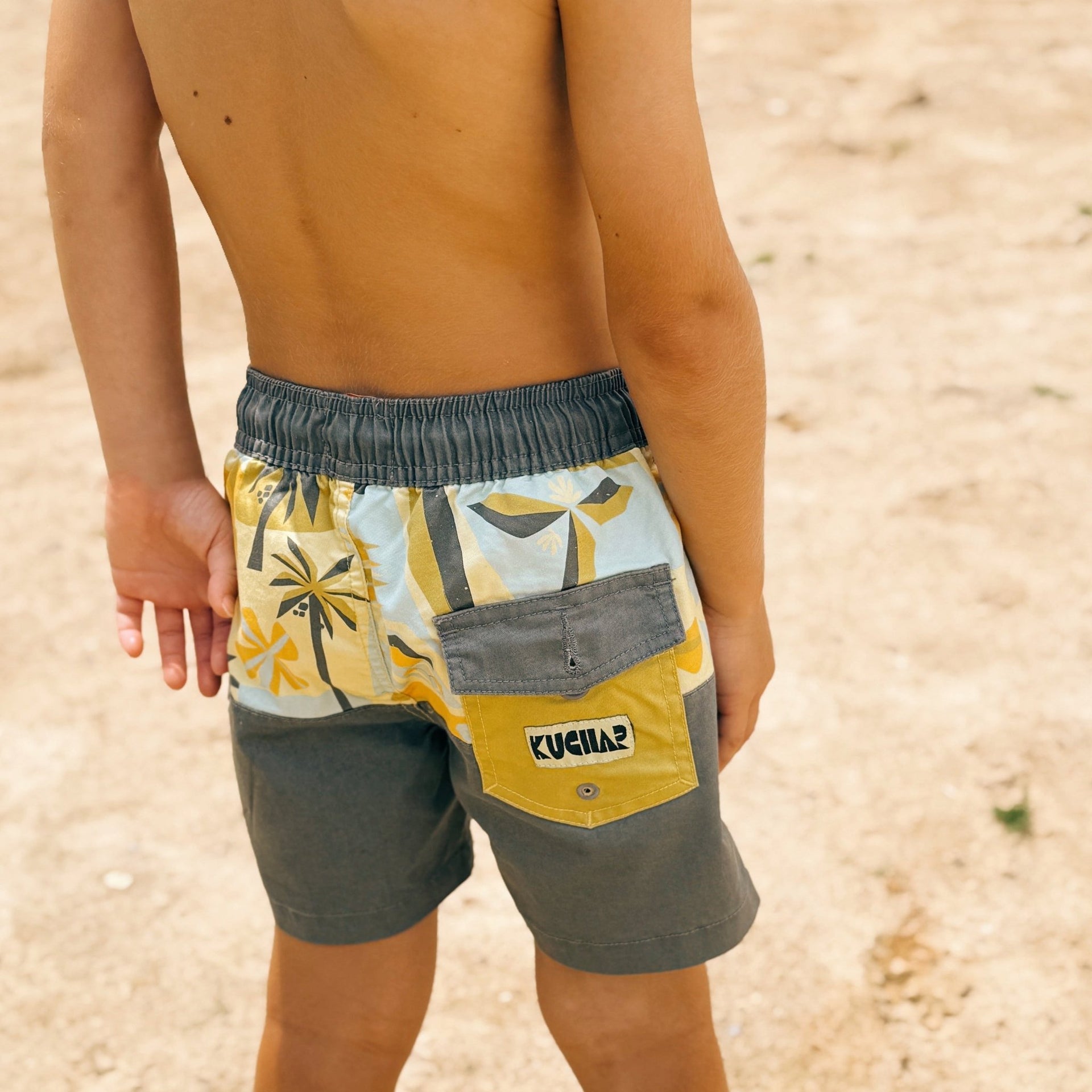 Child wearing a colorful swimsuit with a brand logo on a sandy background