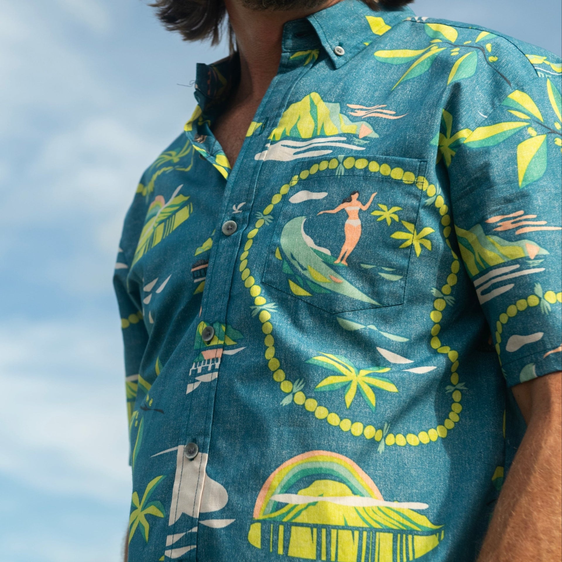 Man wearing a colorful Hawaiian shirt with a scenic design, standing outdoors.