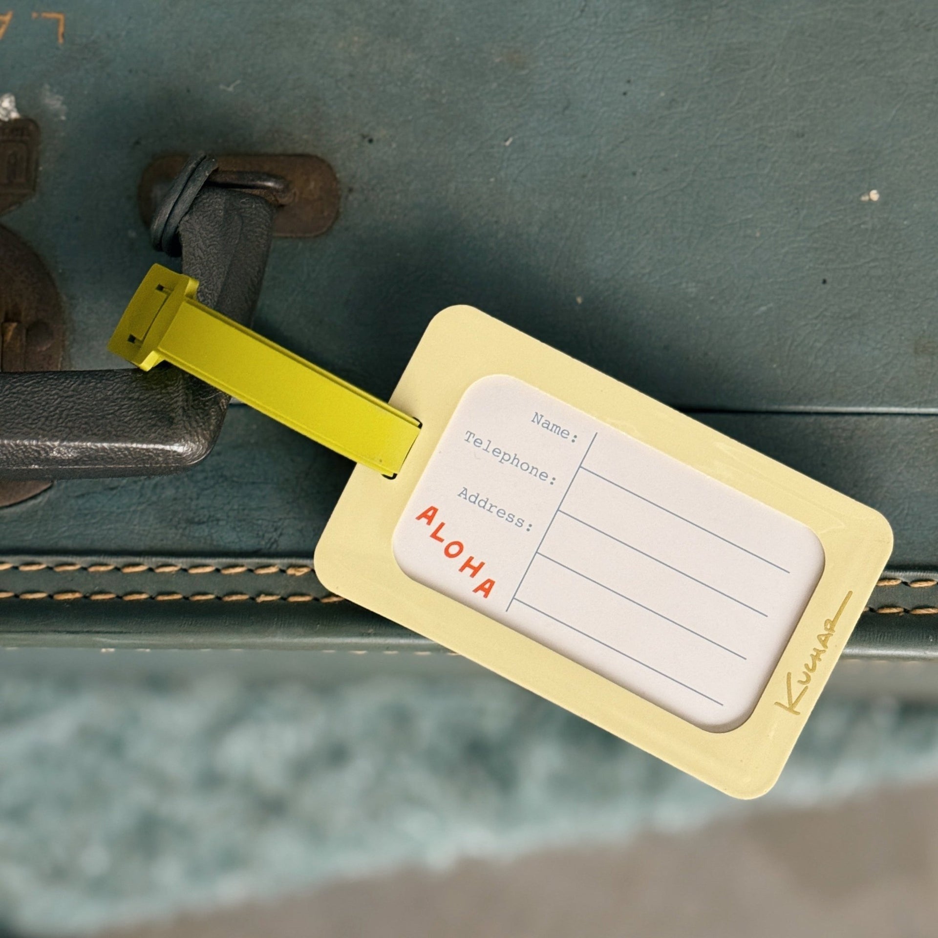 Vintage suitcase with a yellow luggage tag labeled 'Aloha' on a blurred background