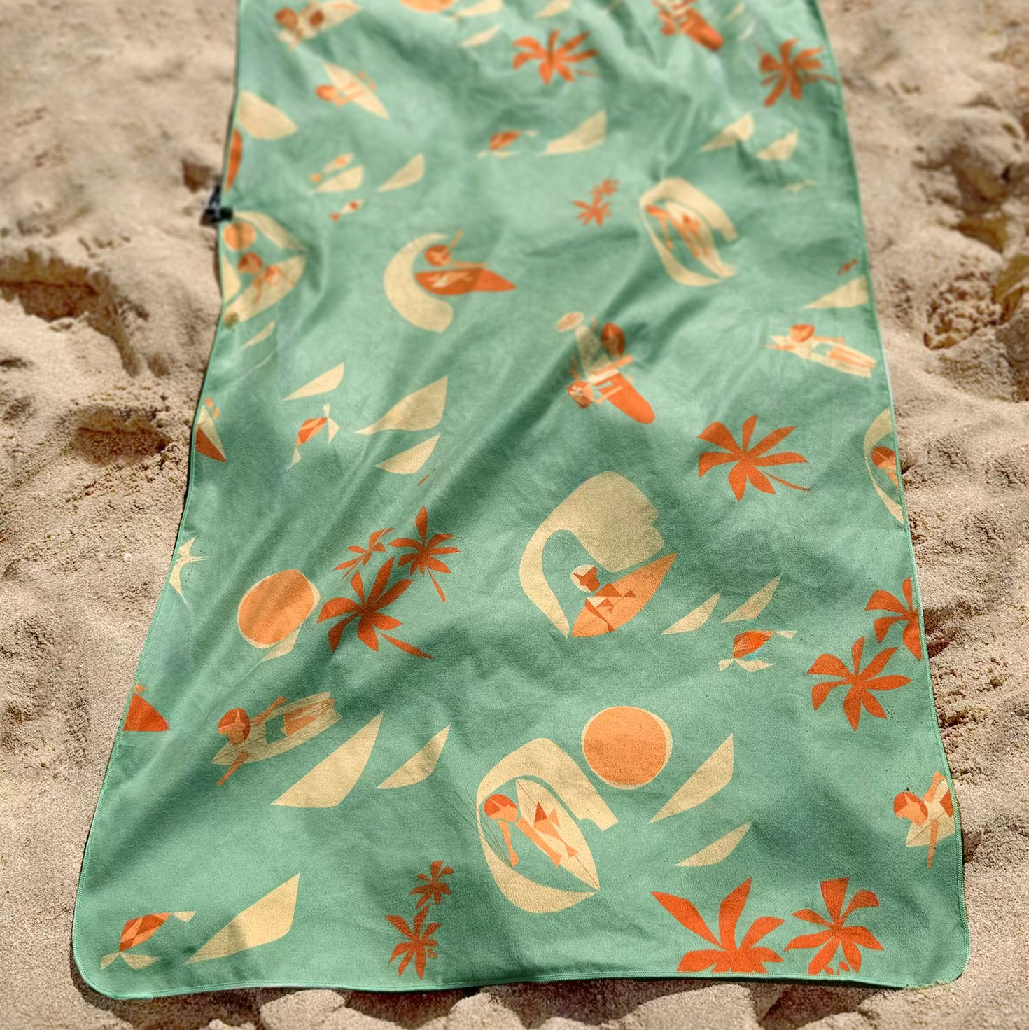 Green towel with nature-themed pattern on a sandy surface