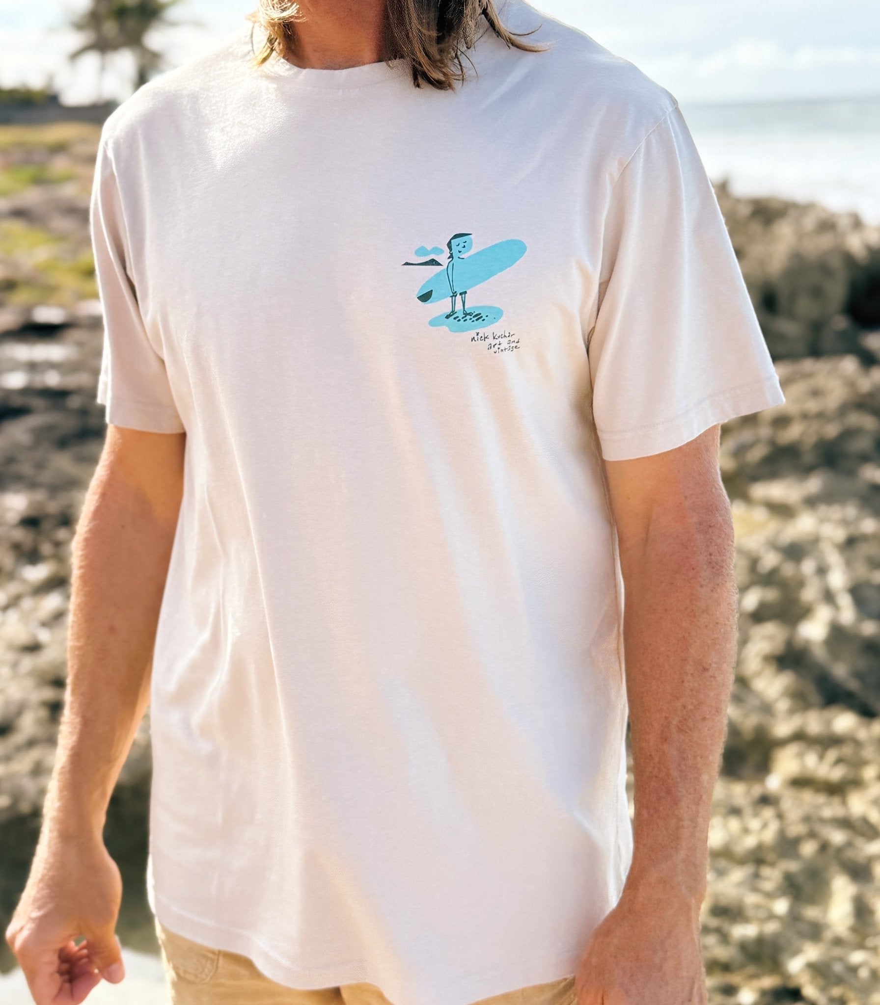 Man wearing a white Hawaii t-shirt with a blue graphic on a rocky beach