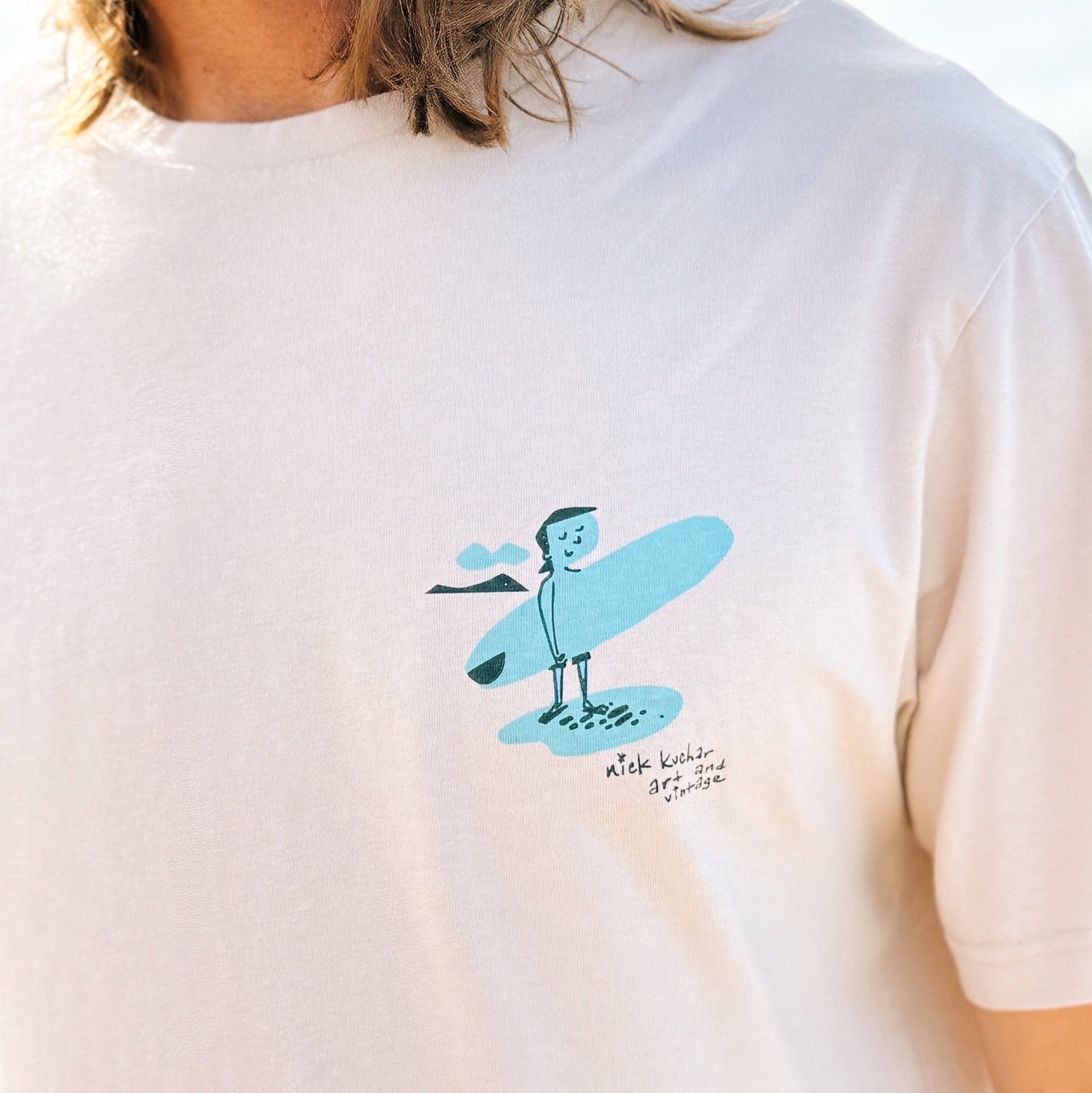 White t-shirt with a blue graphic design on a person wearing it.
