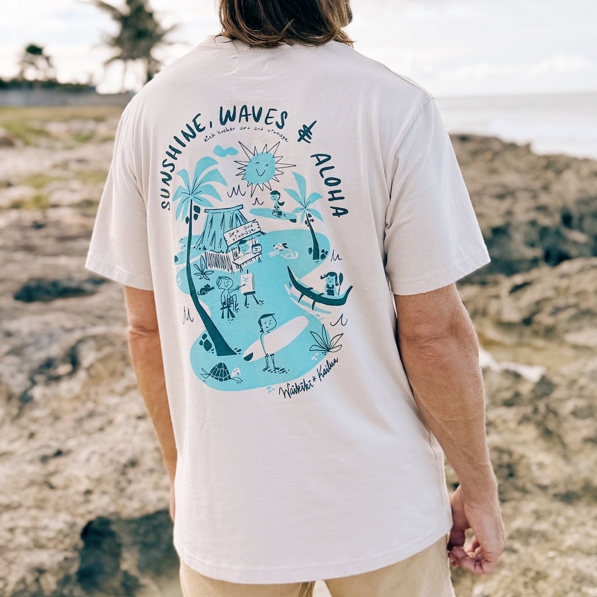 Person wearing a white t-shirt with a blue graphic design on a beach