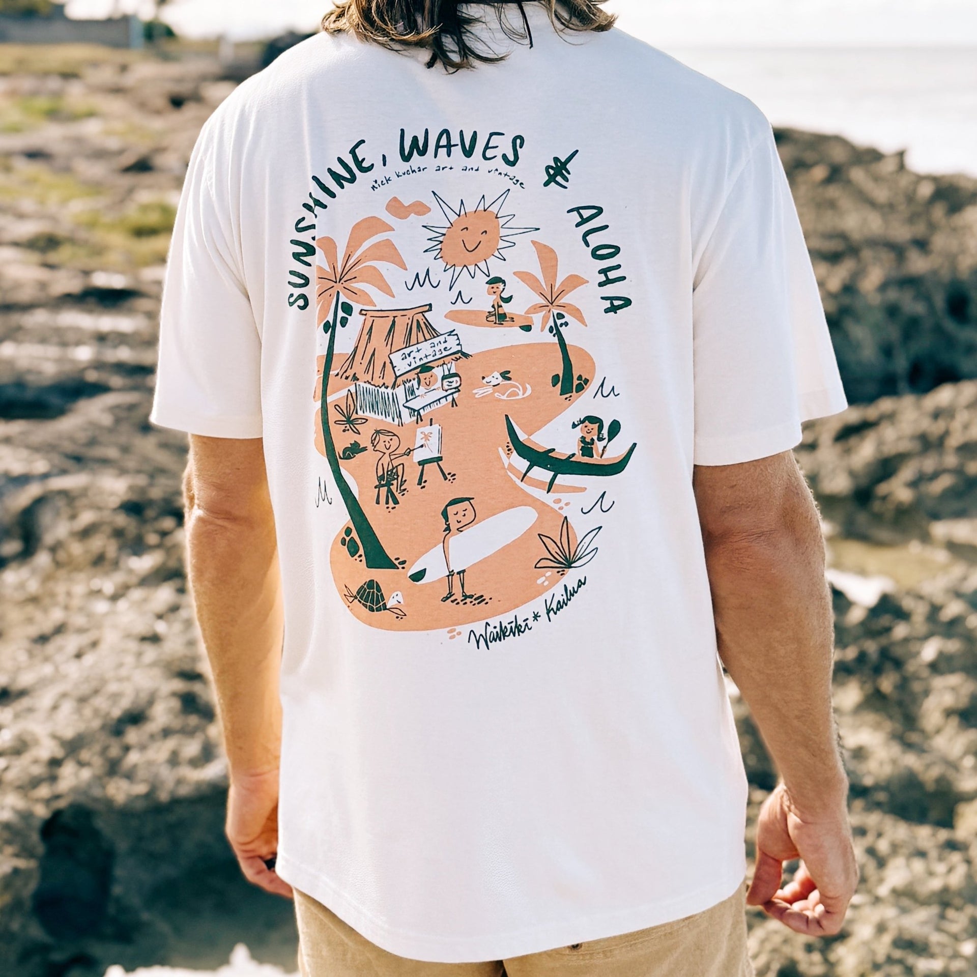 Man wearing a white t-shirt with a beach-themed graphic on a sandy background