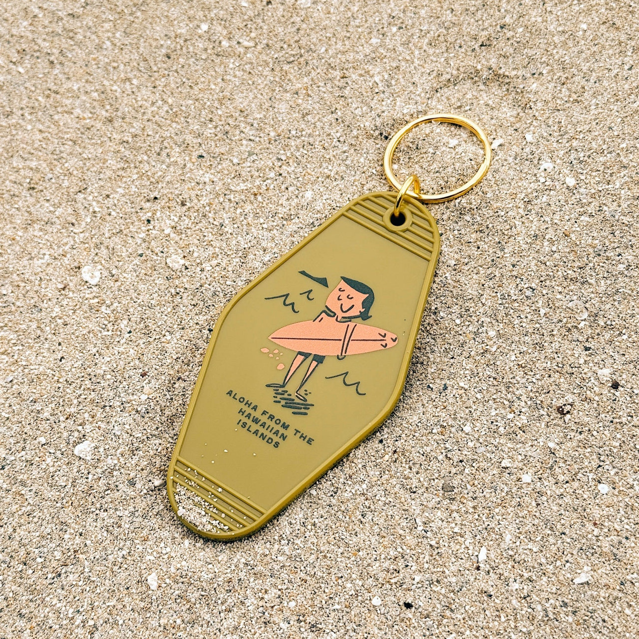 Keychain with a design of a person on a surfboard on a sandy surface