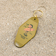 Keychain with a design of a person on a surfboard on a sandy surface