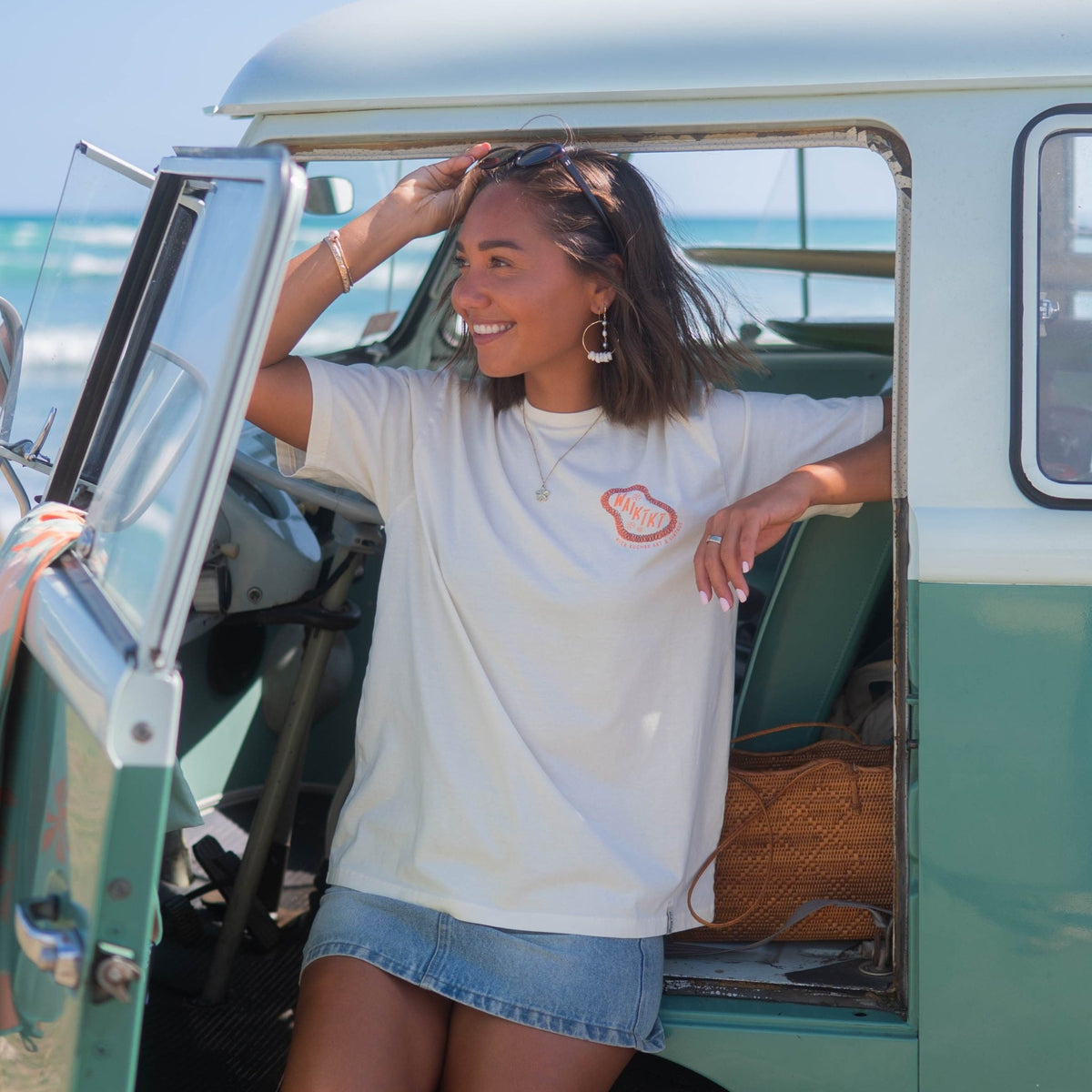 model wearing white waikiki tee shirt next to vintage car at beach